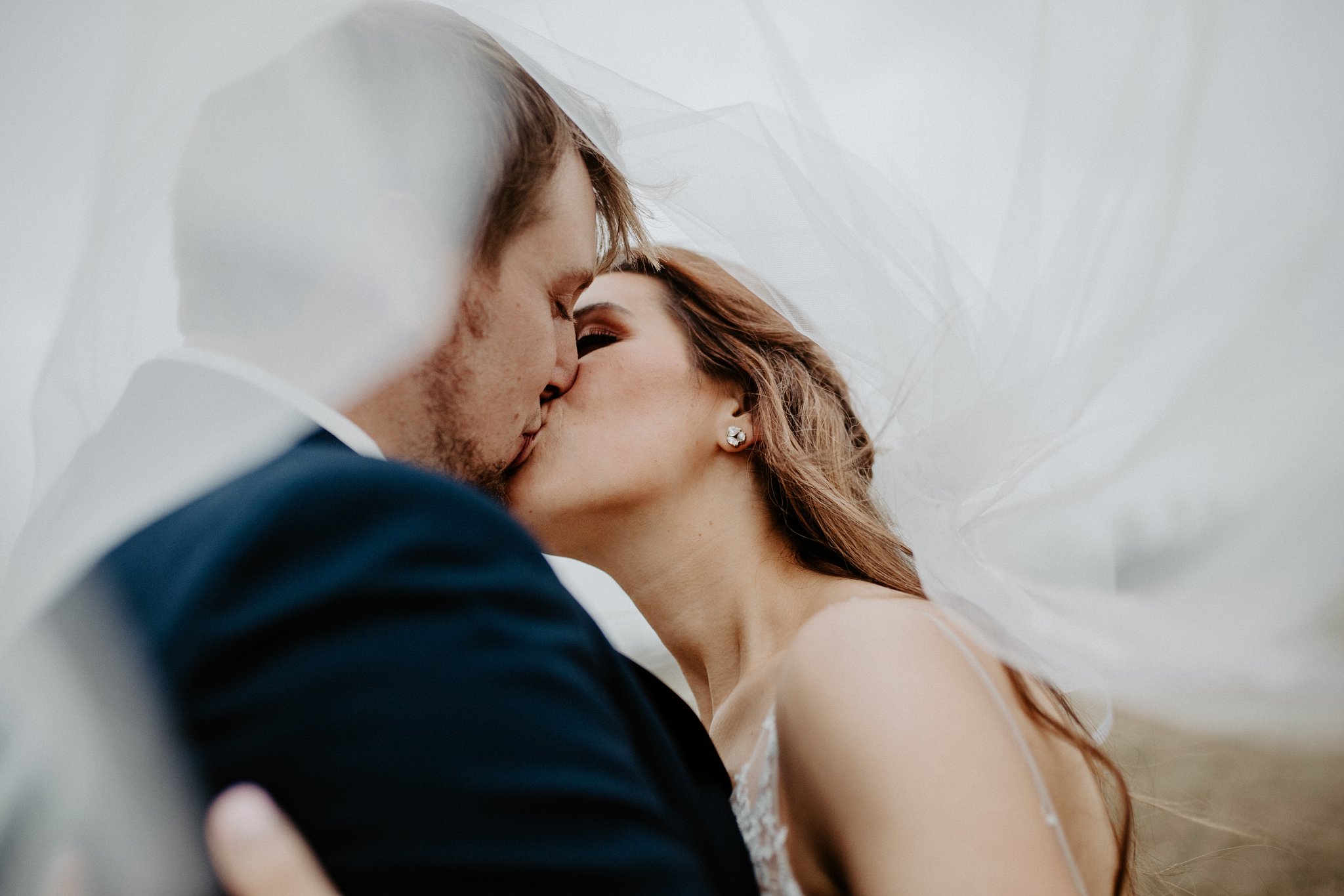 bride and groom kissing while the veil swirls around them