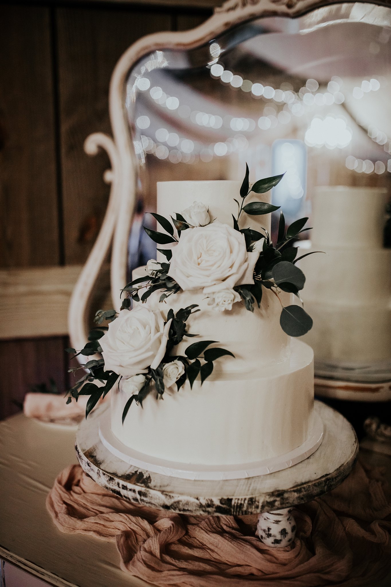 Three tier white wedding cake with white roses and greenery