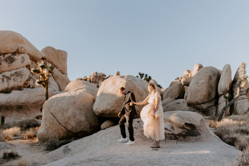A couple is walking on the rocks in Joshua Tree after their elopement ceremony, holding hands and looking down at the ground.