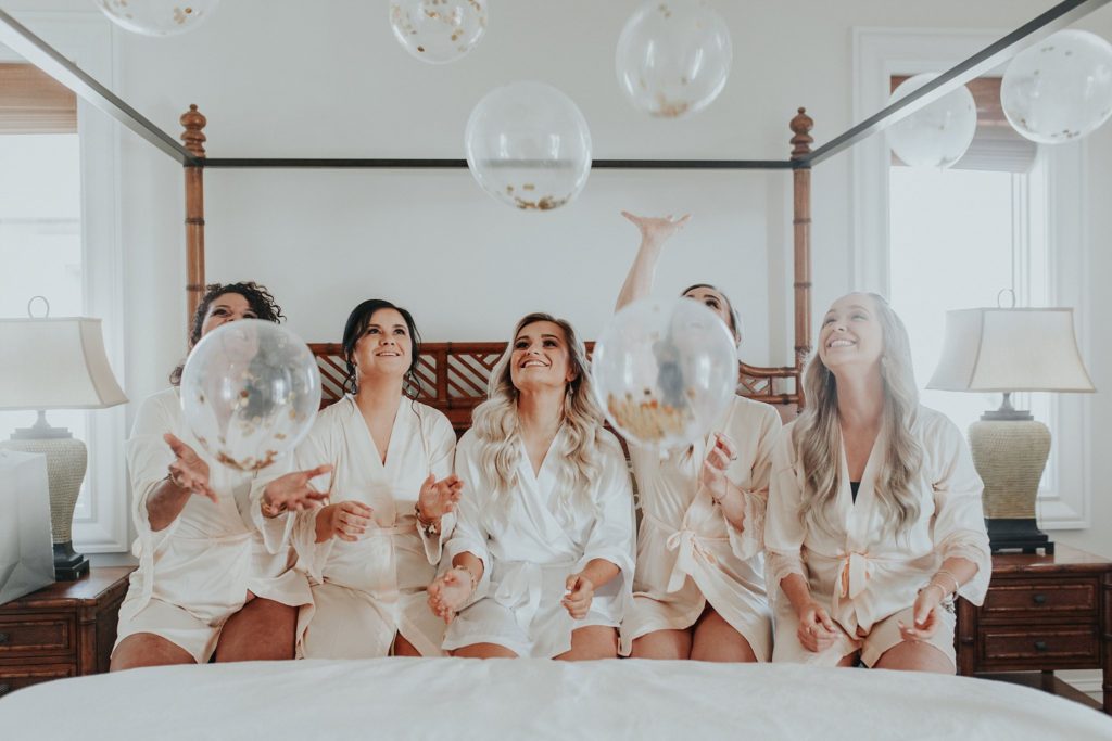 how to have a destination wedding bride sitting on the bed with her bridesmaids bouncing balloons in the air