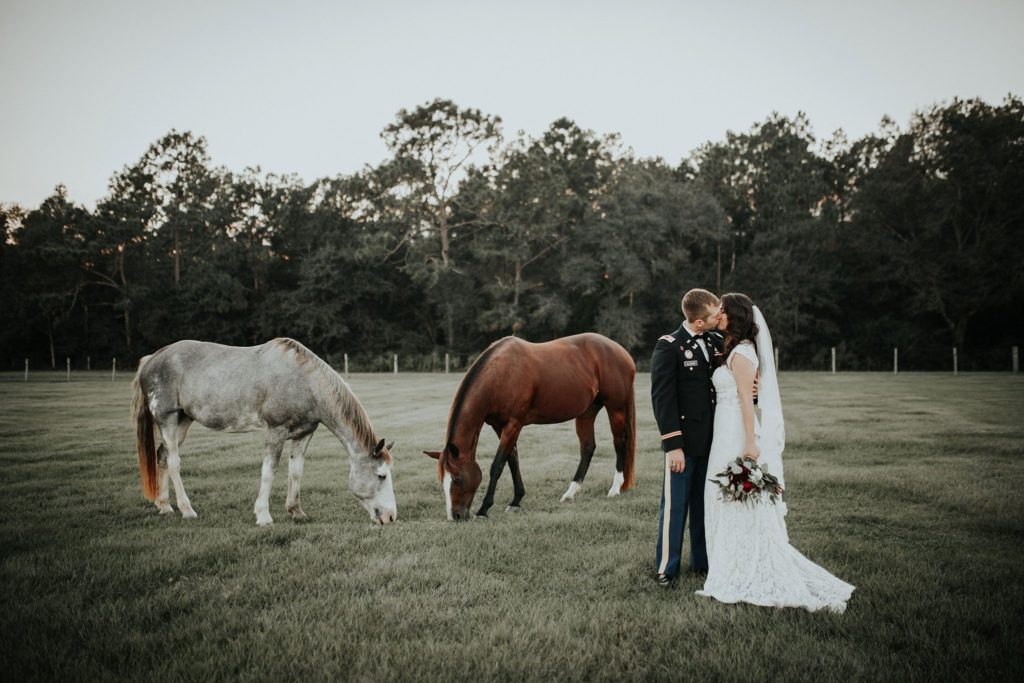 questions to ask wedding photographers bride and groom standing in a field with horses