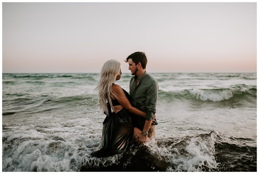 Man in green shirt and woman in black dress gaze into each others eyes while standing in the water on the beach - Rosemary Beach Photographer