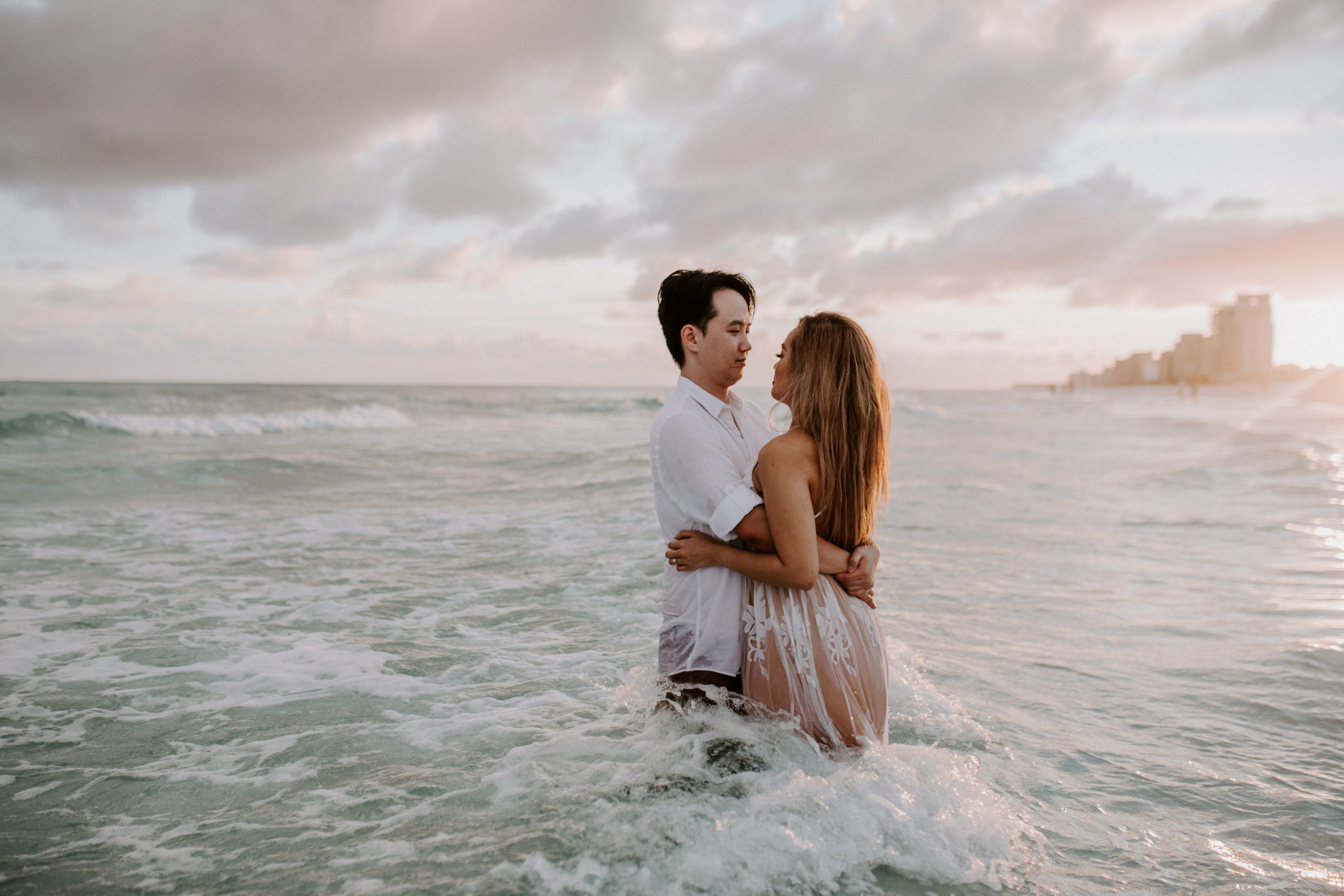 what to do after eloping - man and woman couple stand in the water in wedding clothes letting the waves crash around them