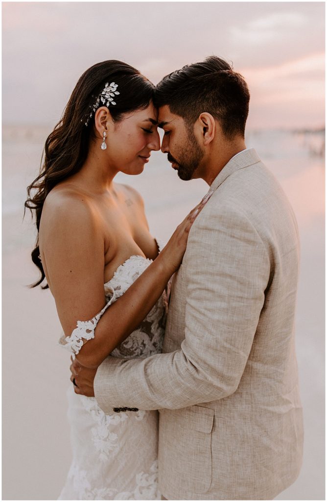 Bride and groom with foreheads together on the beach at sunset