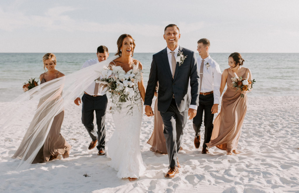 Couple in wedding clothes walking on the beach with their bridal party