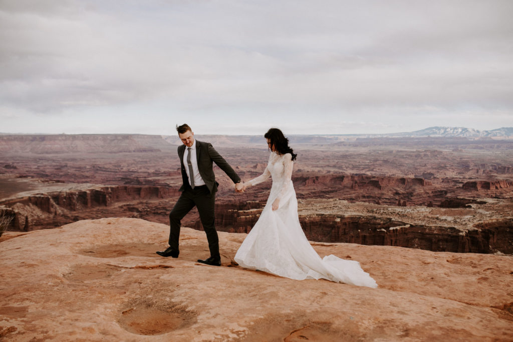 Couple in wedding clothes walking on the edge of a canyon in Moab Utah
