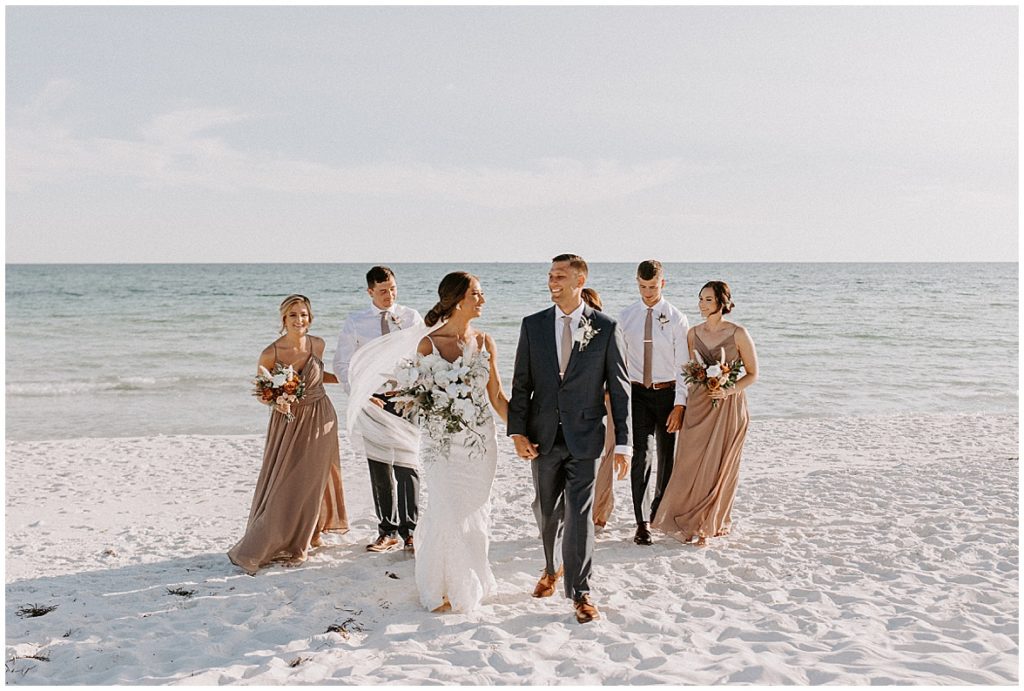 Wedding party walks with the couple on the beach