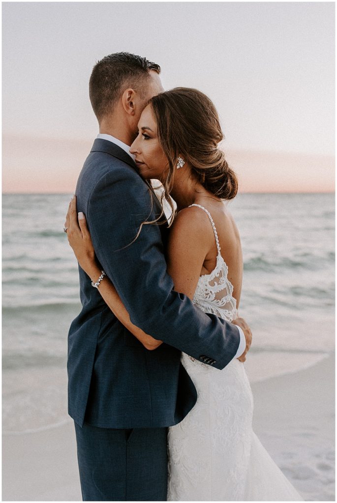 Bride and groom hug on the beach at sunset