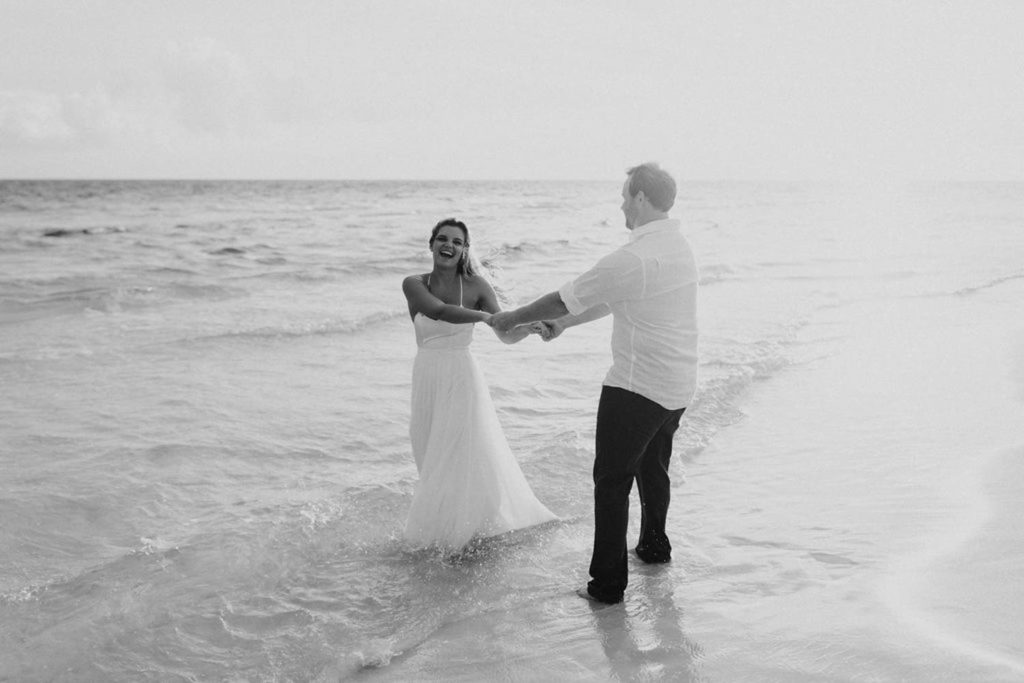 A couple is dancing on the beach on their elopement day, holding hands and laughing.