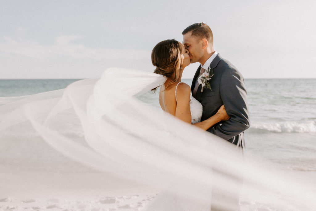 A couple is kissing on the beach during their all day elopement.