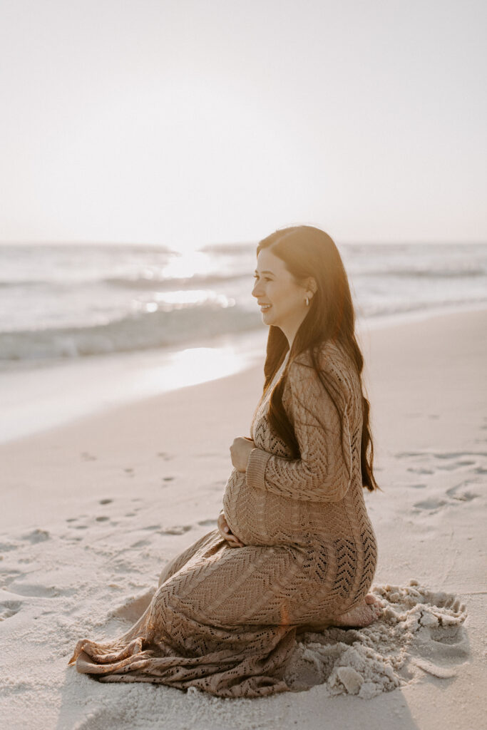 Pregnant woman sitting on her knees on the beach during her Destin maternity photography session