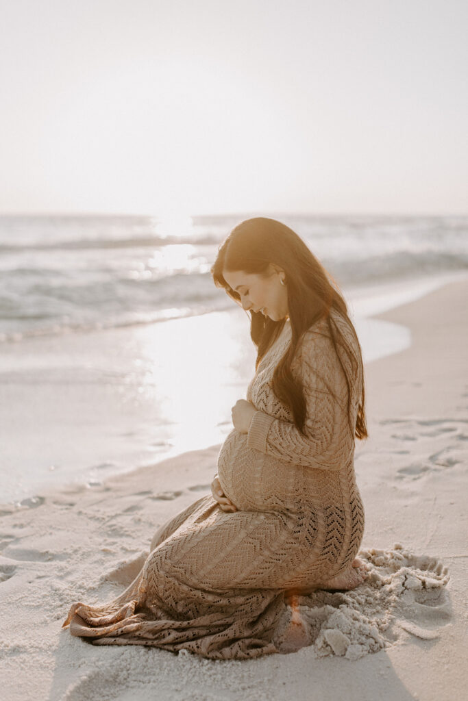 Pregnant woman sitting on her knees on the beach during her Destin maternity photography session