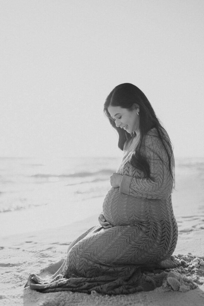 Pregnant woman sitting on her knees on the beach during her Destin maternity photography session