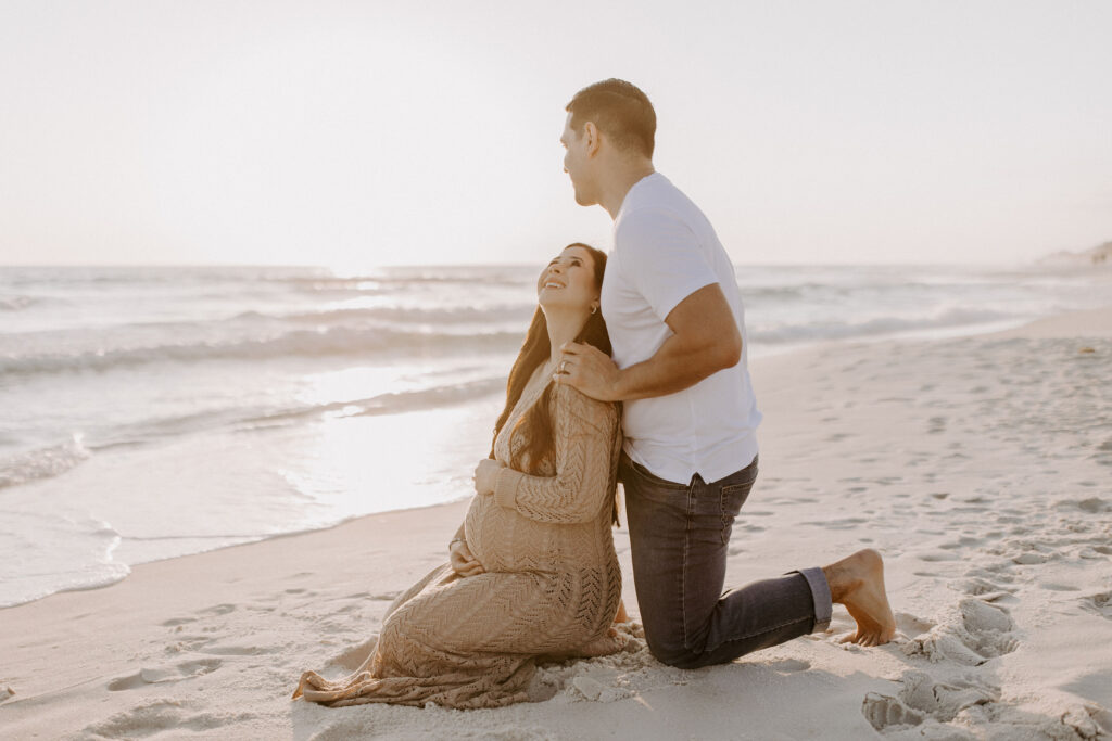 Couple sitting on their knees on the beach during her Destin maternity photography session