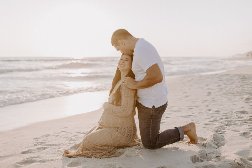 Couple sitting on their knees on the beach during her Destin maternity photography session