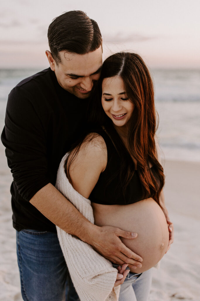 Couple cuddling on the beach during their destin maternity session