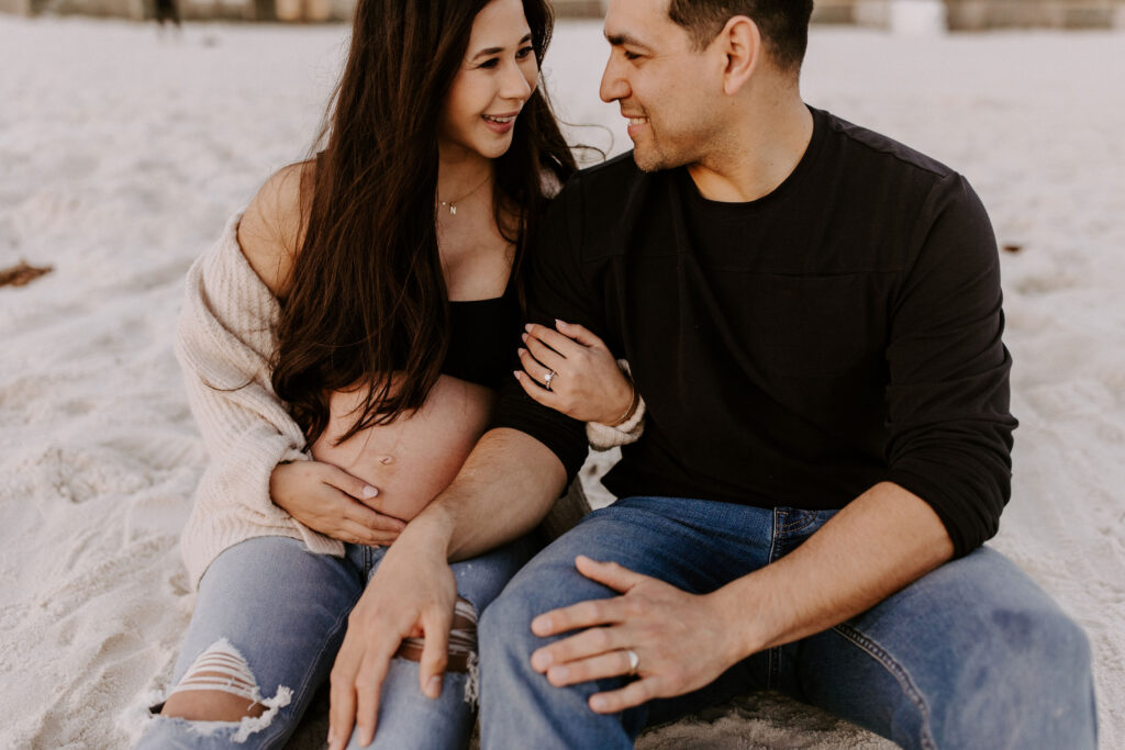 Couple sitting on the beach at their Destin maternity photography session