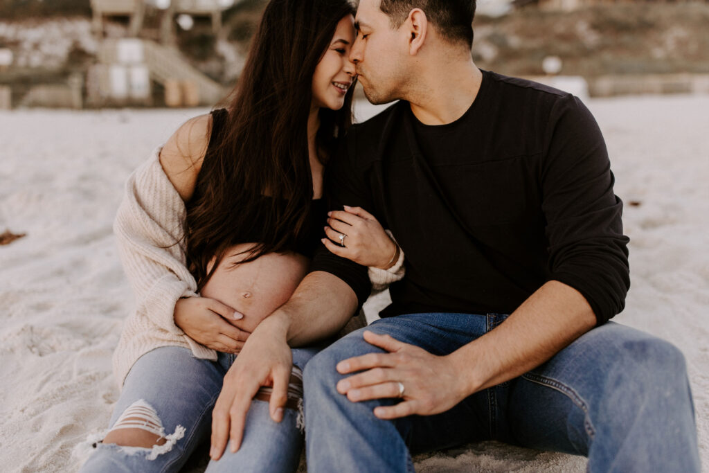 Couple sitting on the beach at their Destin maternity photography session