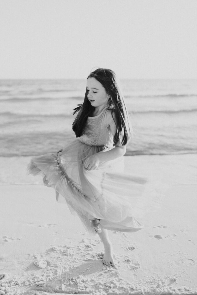 Black and white photo of child twirling on the beach