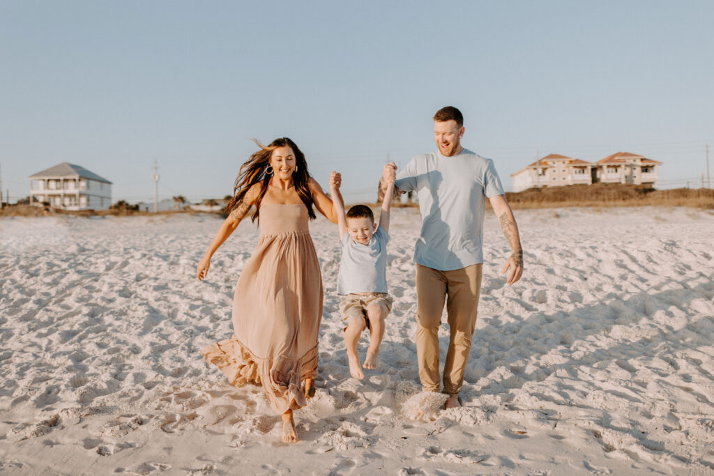 Mom and dad swinging a little boy between them on the beach